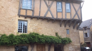 A traditional half-timbered building with stone walls and wooden beams. There are multiple windows with shutters, a wooden door, and a small outdoor seating area with a table and chairs. - Beautiful Périgourdine house with pool access Hôtel La Roseraie (Montignac-Lascaux)