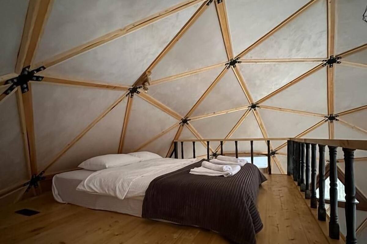 Quarto tipo tenda com cama, piso de madeira e vista da estrutura ao redor.