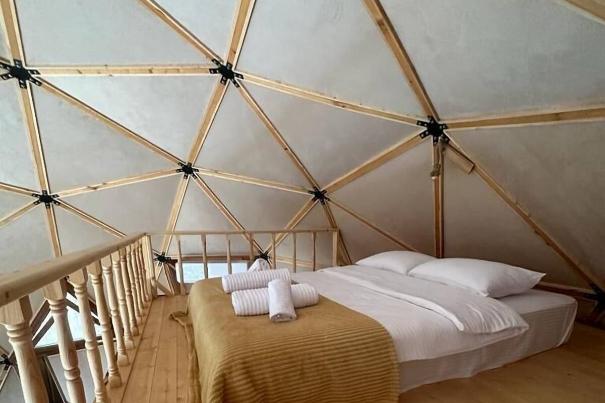 Uma tenda de madeira triangular com cama, soalho de madeira e guarda-corrimão.