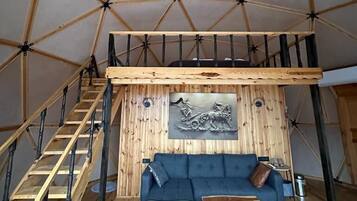 A spacious tent with a lofted sleeping area, a wooden staircase, a couch, and a patterned rug.