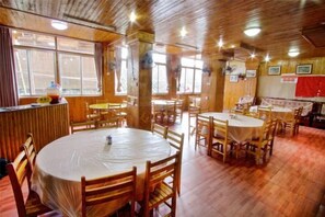 Zona pranzo con tavoli e sedie rotonde, pavimento in legno e bancone bar.