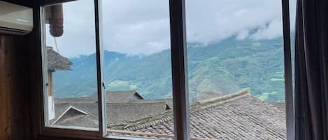 A room with a large window overlooking a mountainous landscape with traditional buildings.