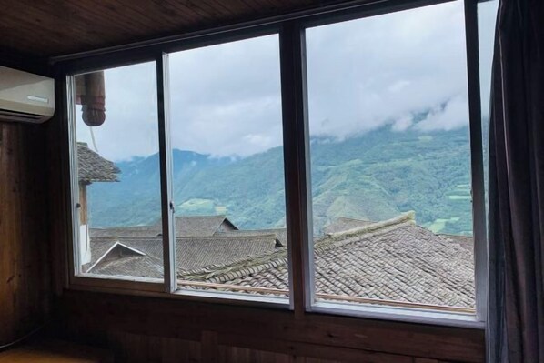Una habitación con un amplio ventanal que da a un paisaje montañoso con edificios tradicionales.