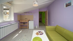 Un espace de vie compact comprenant un coin cuisine, un canapé vert et un tapis à motifs.