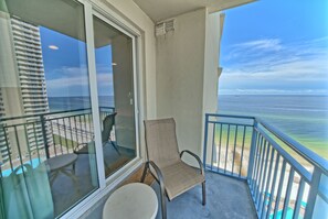 A balcony with a chair and table, overlooking a beach and ocean. - Ocean Breeze (Panama City Beach)