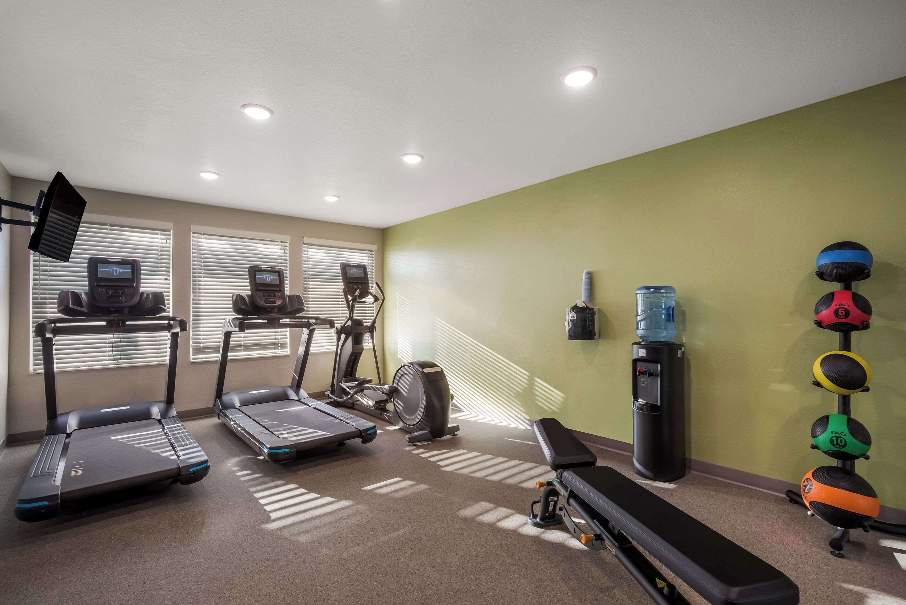 Un gimnasio con cintas de correr, una elíptica, un dispensador de agua y un banco.