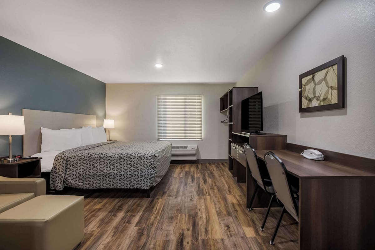 A hotel room with a bed, desk, chairs, a telephone, and a window with blinds.