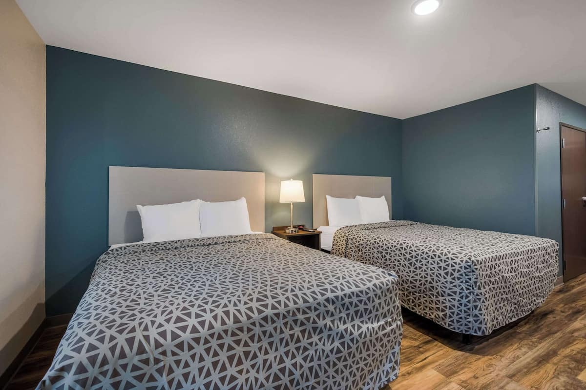 A hotel room with two beds, a nightstand with a lamp, and a wooden floor.
