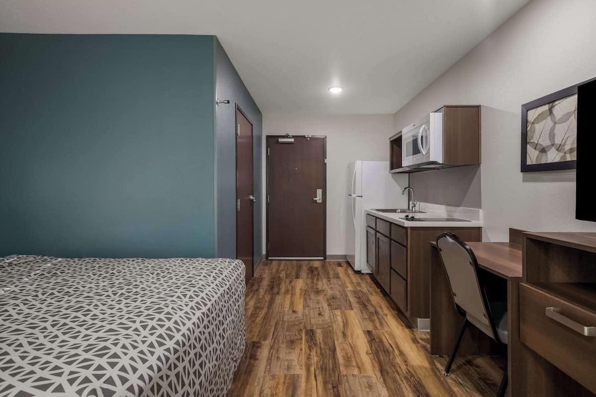 A compact room with a bed, a kitchenette, and a door leading to another room.