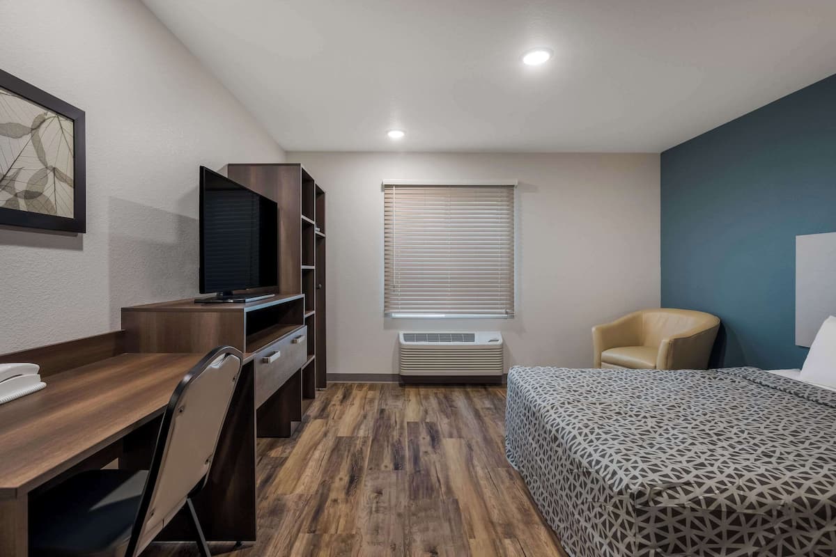 A hotel room with a desk, chair, bed, and a window with blinds.