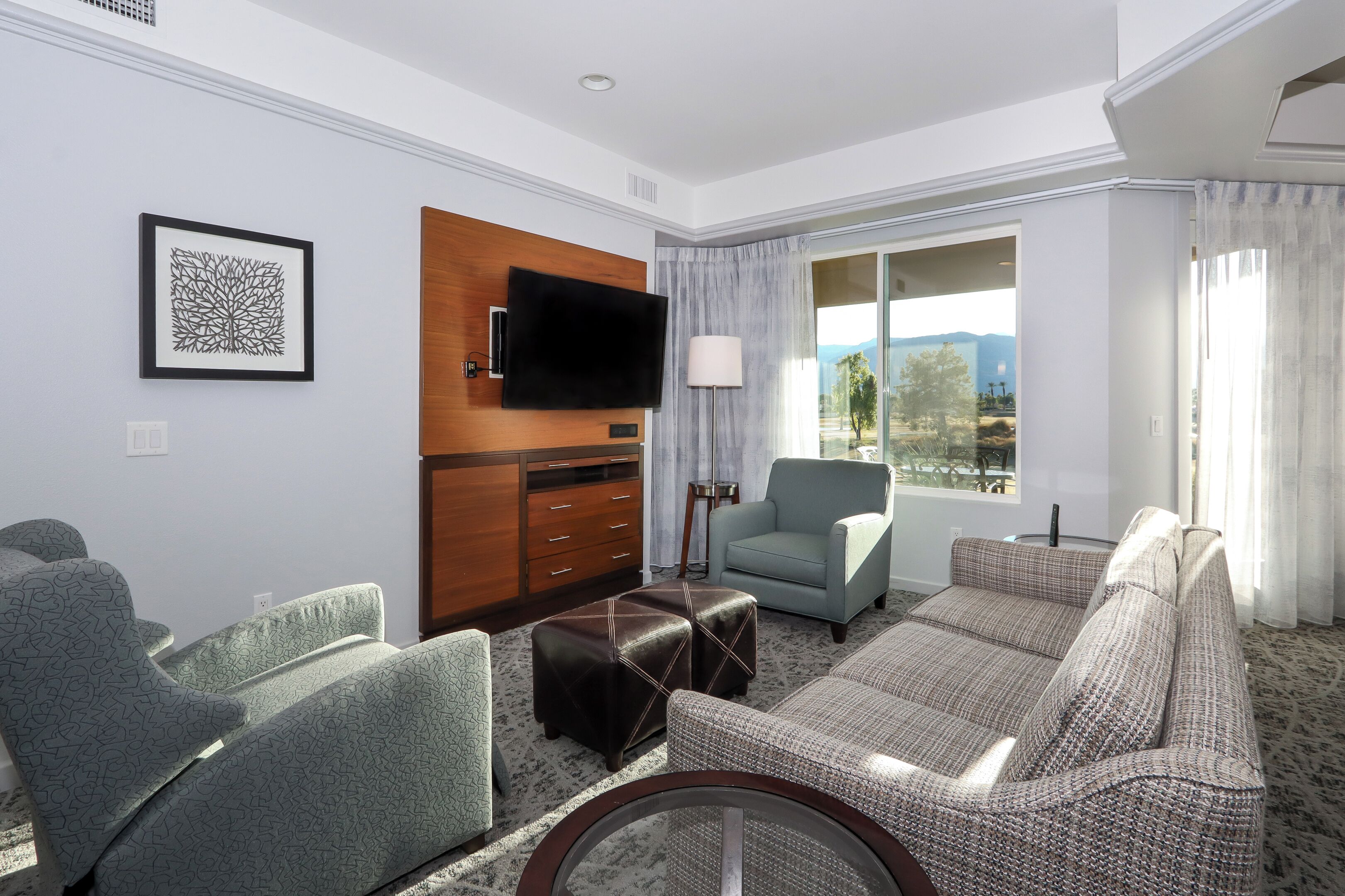 Une chambre d’hôtel équipée d’une télévision à écran plat, d’une armoire en bois, d’un canapé, d’un fauteuil et d’une fenêtre donnant sur les montagnes.