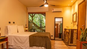 Ein Schlafzimmer mit einem Bett, einem Nachttisch, einem Deckenventilator, einem Fenster mit Blick auf Bäume und einem Holzschrank mit einer Pflanze.