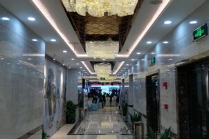 Un pasillo de hotel con candelabro, paredes de mármol y suelo estampado.