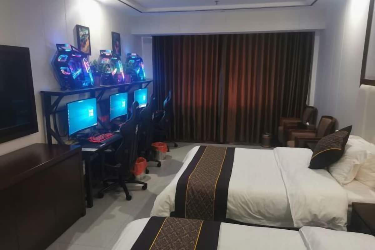 A hotel room with a bed, a desk with multiple monitors, and a TV.