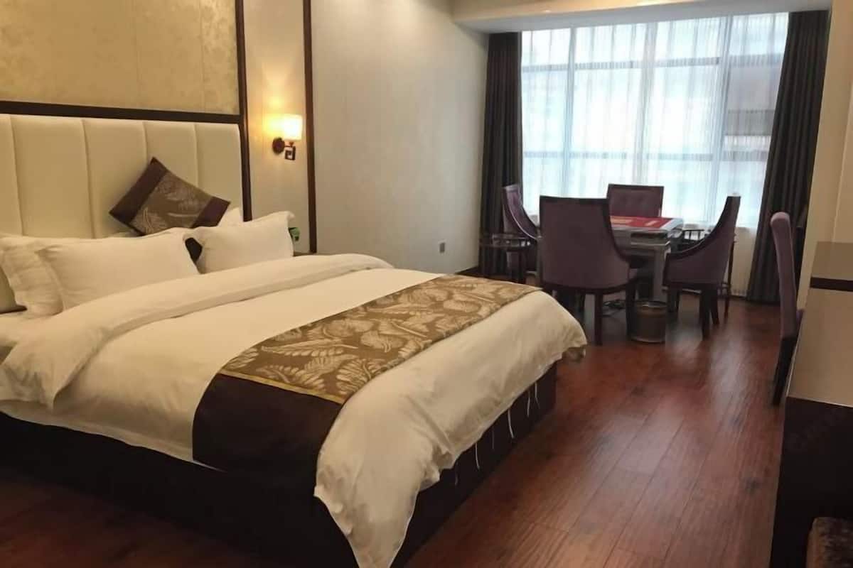 A hotel room with a large bed, a desk with two chairs, and a window with curtains.