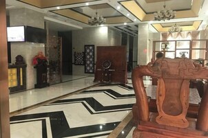A lobby with a black and white patterned floor, a wooden reception desk, and a chandelier.