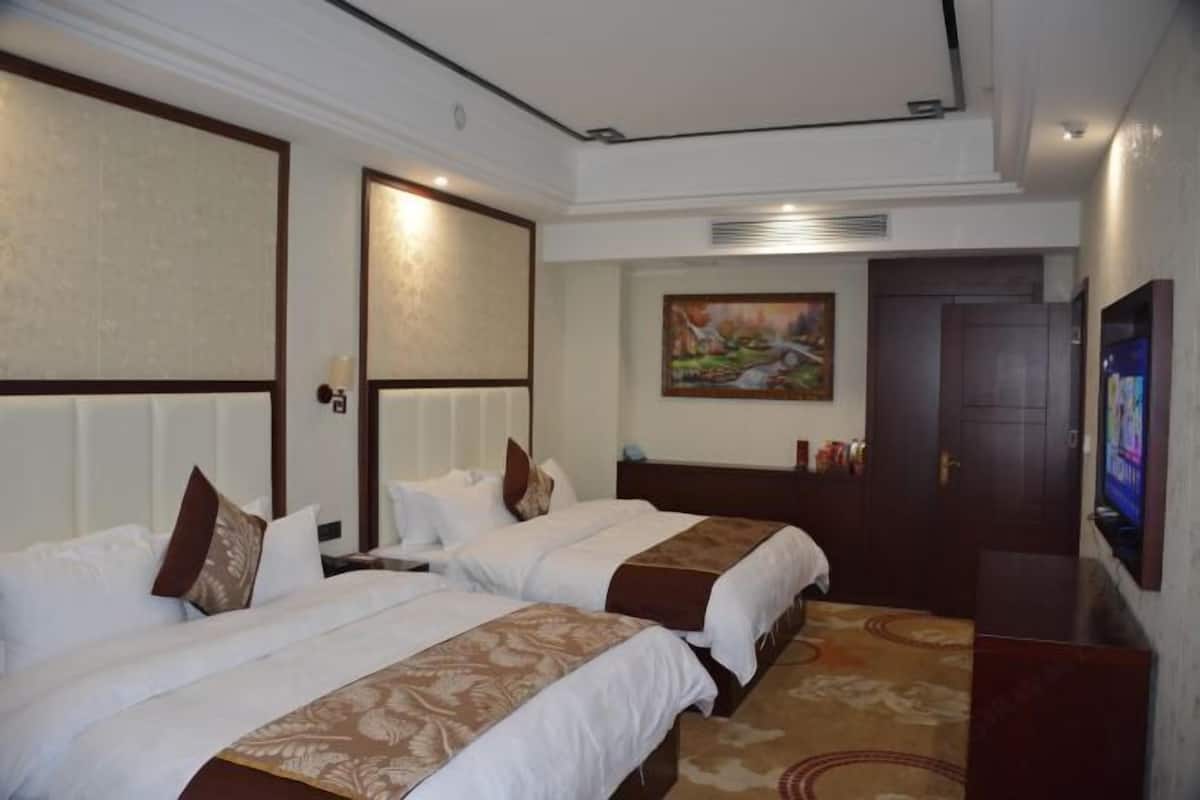 A hotel room with two beds, a painting on the wall, a television, and a door.