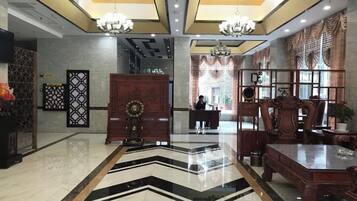 A hotel lobby with a reception desk, a large wooden cabinet, and a chandelier.