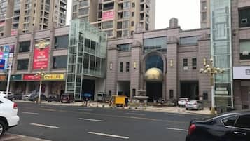 A multi-story building with a large arched entrance, a glass facade, and a street in front with parked cars.