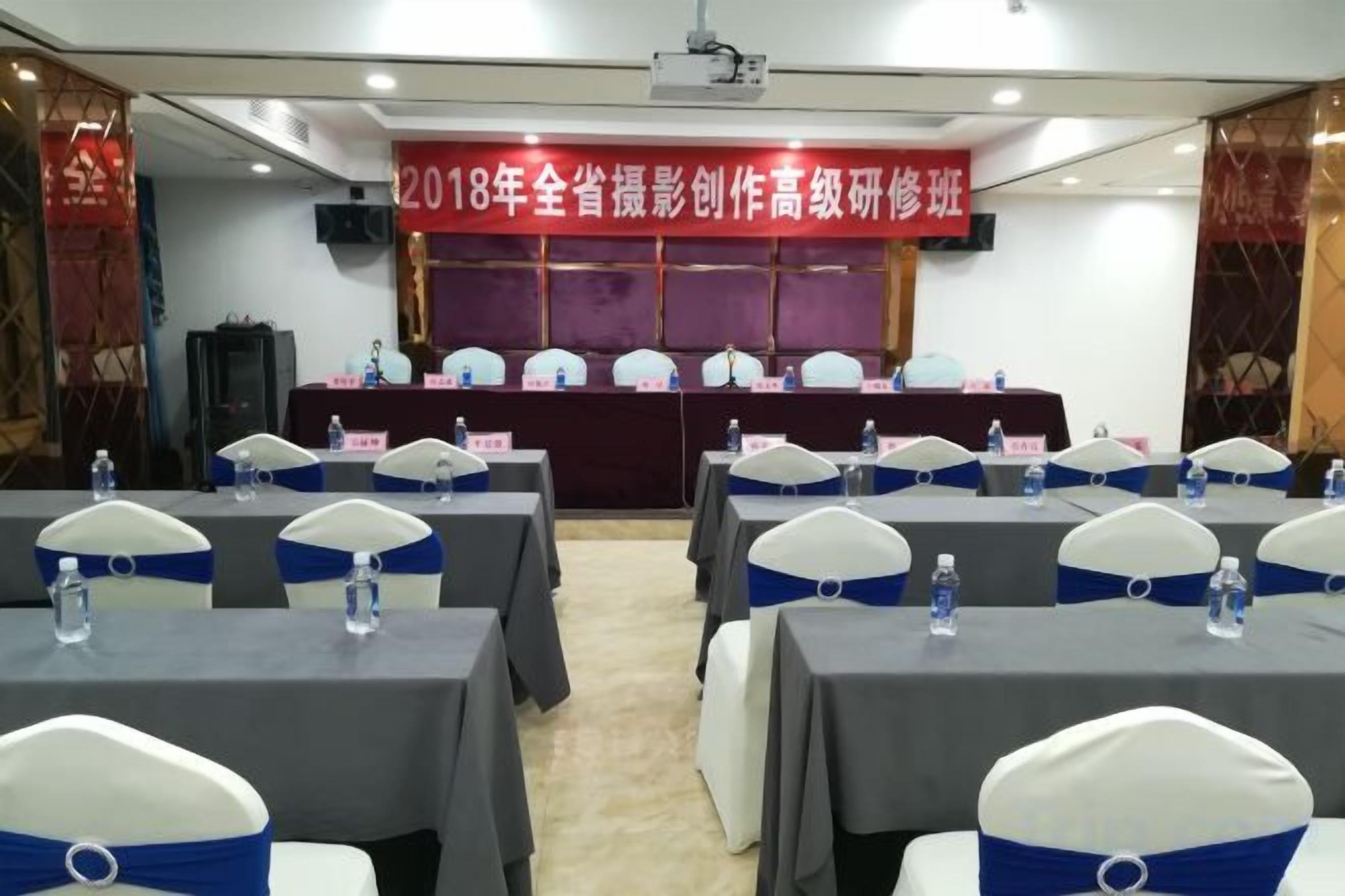 Un salón de conferencias con mesas, sillas, un cartel y una pantalla para proyector.