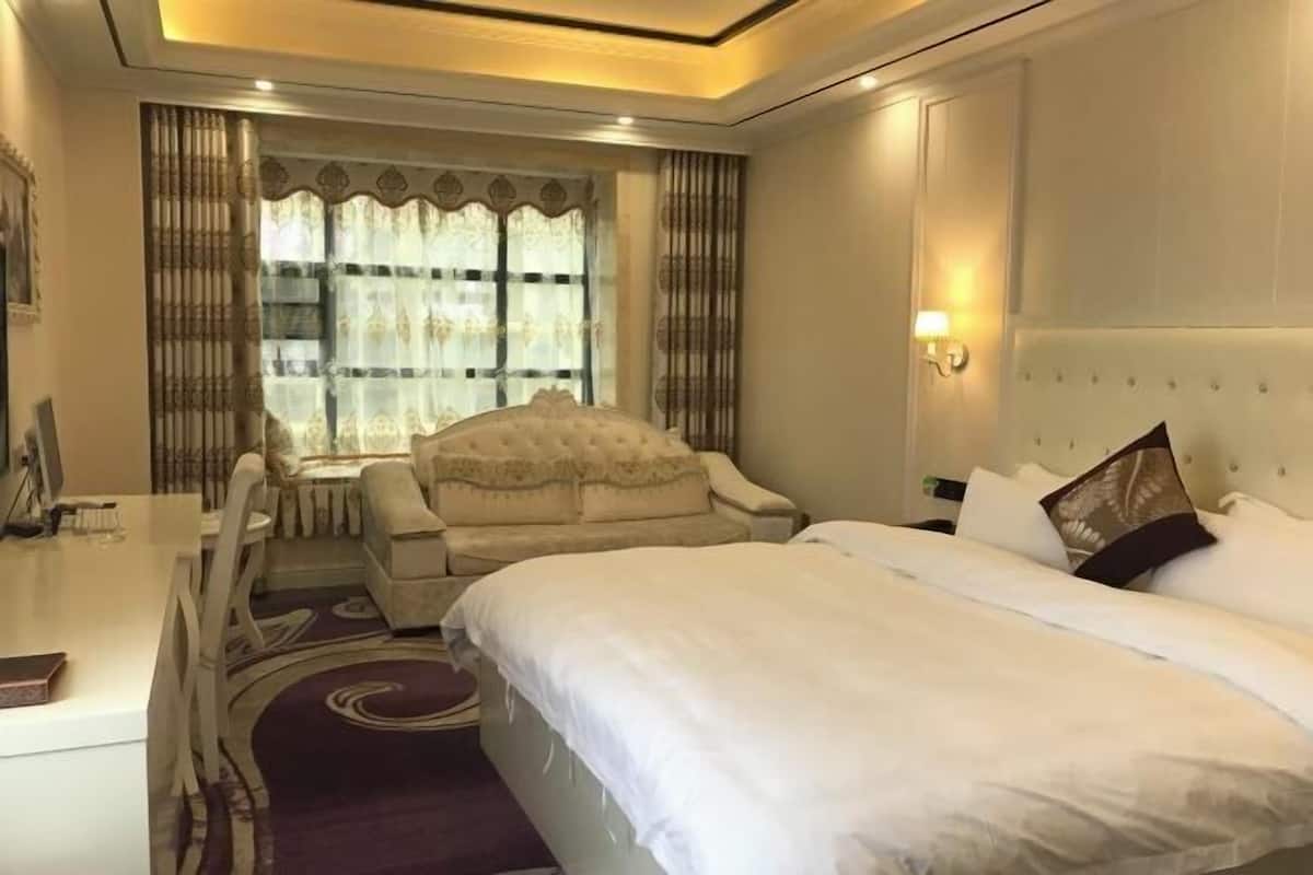 A hotel room with a large bed, a sofa, a desk, and a window with curtains.