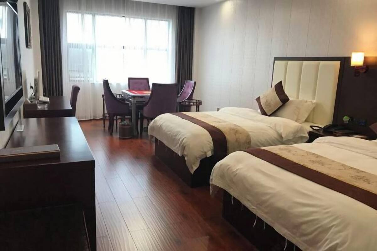 A hotel room with two beds, a desk with chairs, a TV, and a window with curtains.
