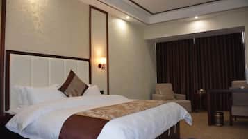 A hotel room with a large bed, a sitting area with a chair and a table, and a curtain-covered window.