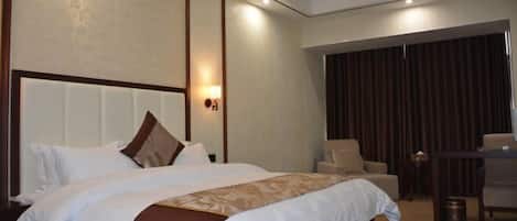 A hotel room with a large bed, a sitting area with a chair and a table, and a curtain-covered window.