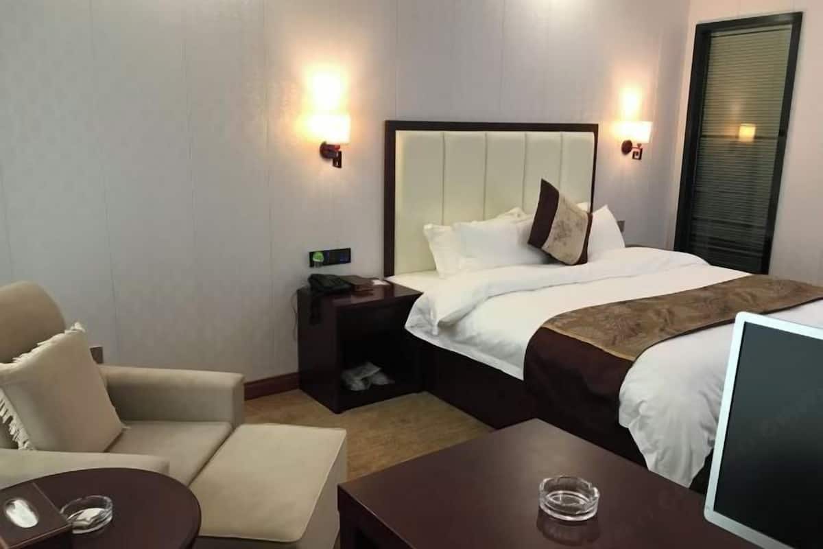 A hotel room with a bed, a desk, a chair, and a bedside table.