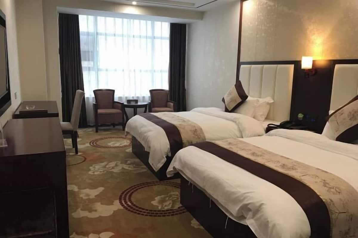 A hotel room with two beds, a desk, a chair, and a small table.