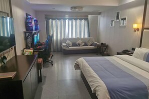 A hotel room with a bed, a desk with a computer, a TV, and a sofa. - Wangxinge Hotel (Nan County)