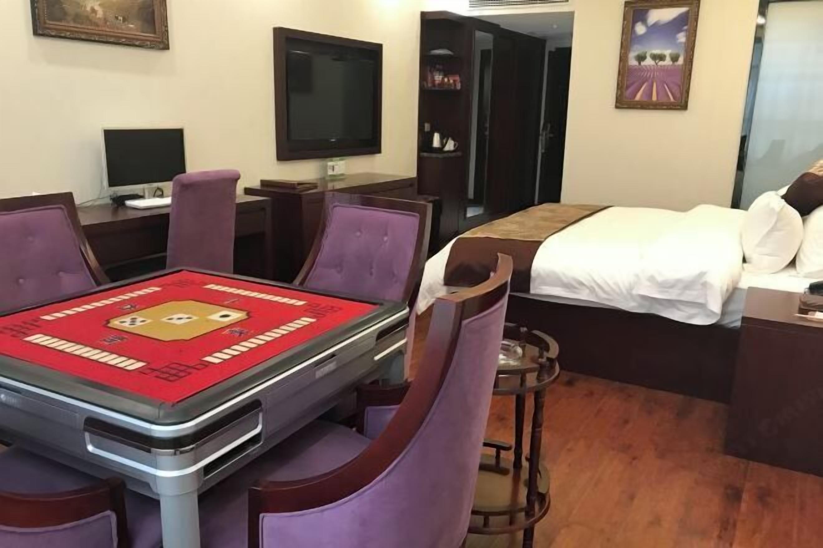 A hotel room with a bed, a desk with a computer, a television, and a table with a red tablecloth.