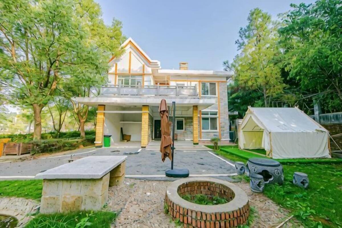 Een tweelaags huis met een balkon, een vuurkorf en een tent in de voortuin.