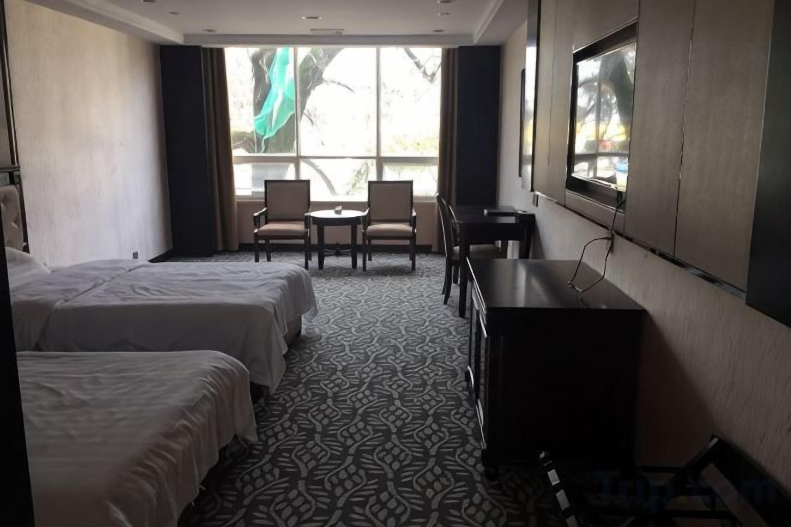 A hotel room with two beds, a desk, a chair, and a window with a view.