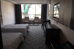 Habitación de hotel con dos camas, un escritorio, una silla y ventana con vistas.