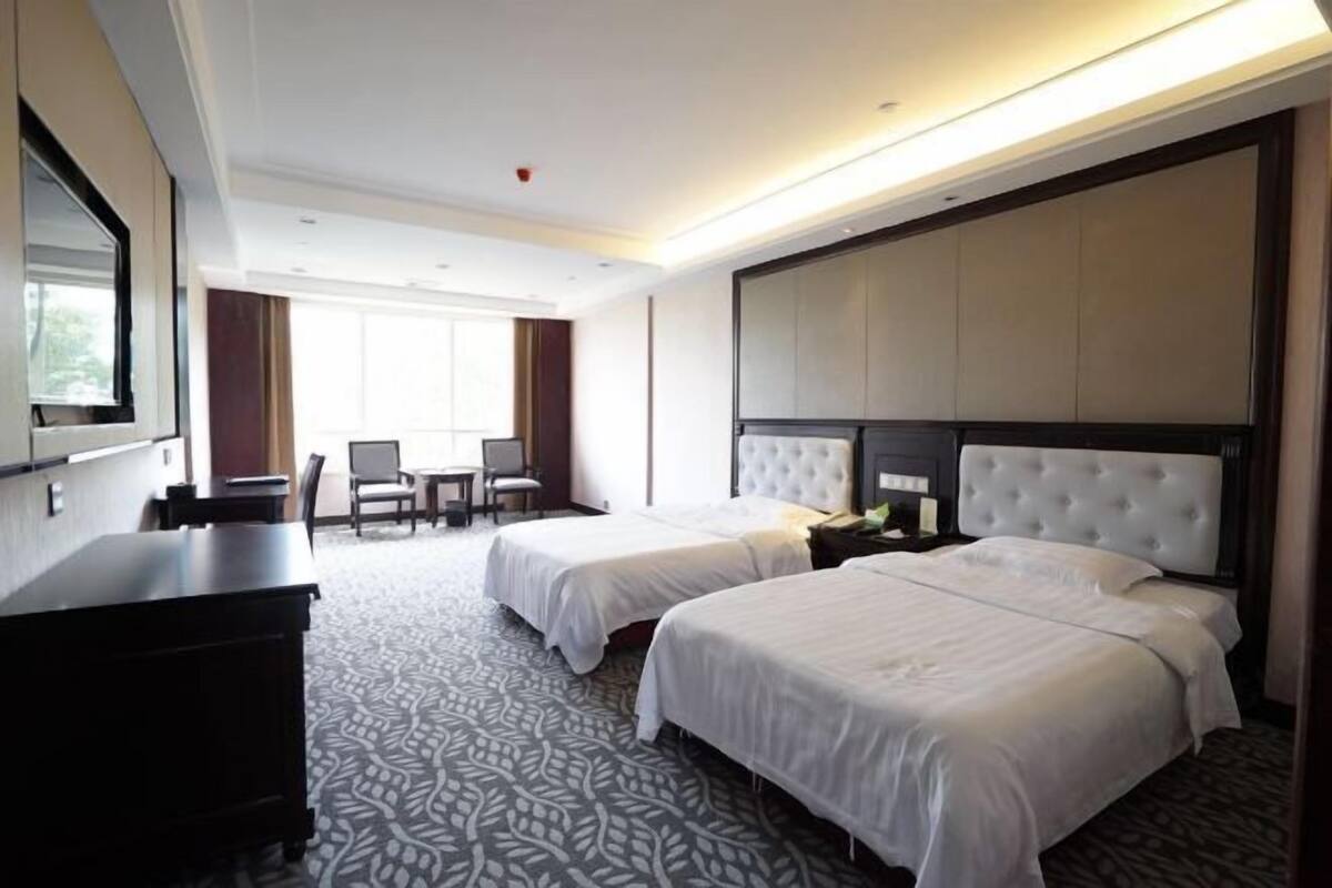 Een hotelkamer met twee bedden, een bureau, een stoel en een groot raam.