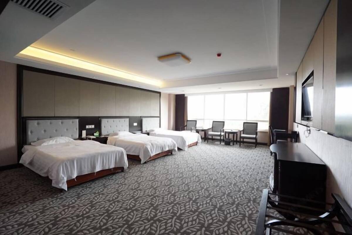 Hotelkamer met drie bedden, een bureau, een televisie en een groot raam.