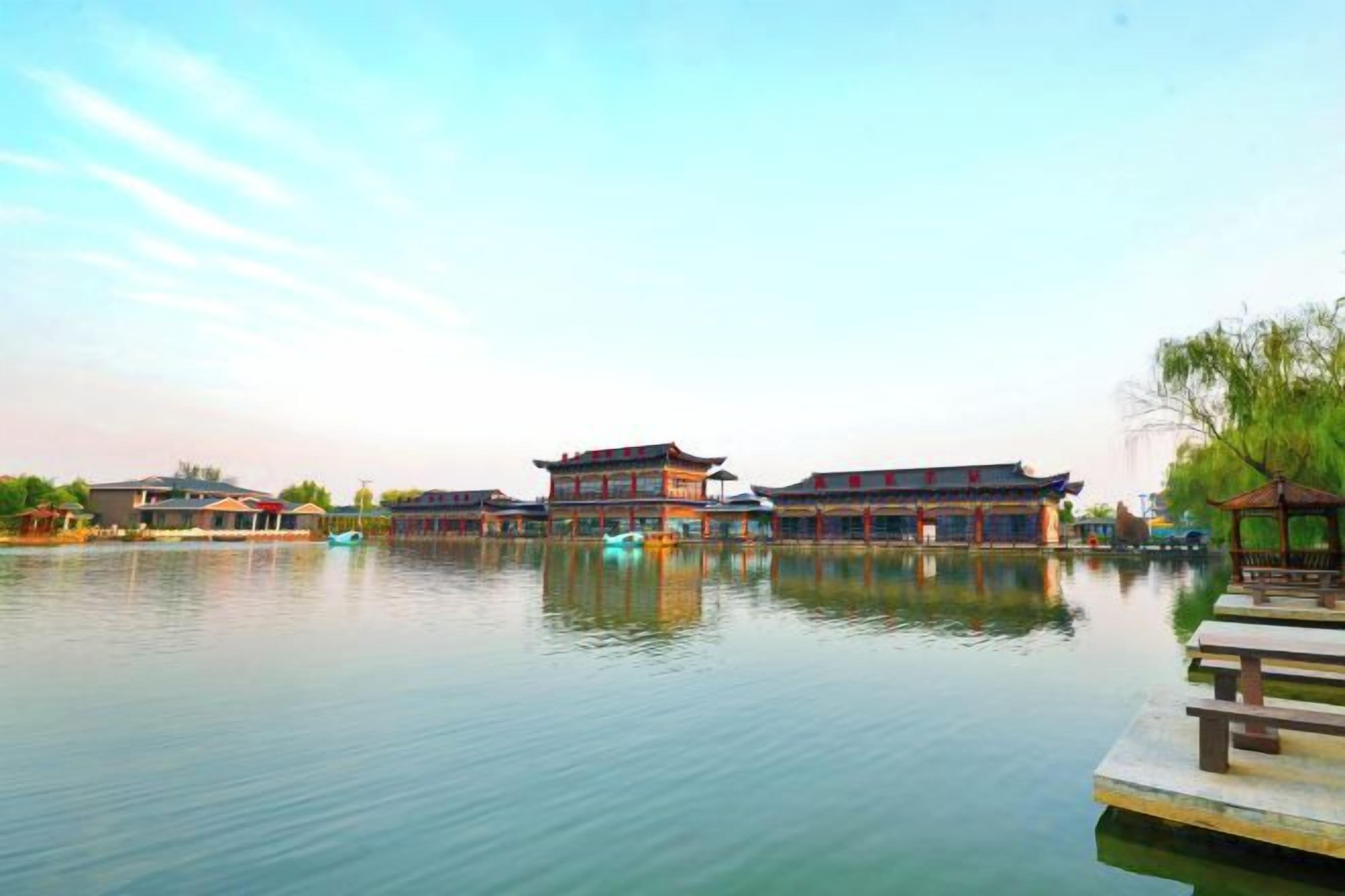 A traditional building with a reflection in calm water, a dock, and a gazebo.