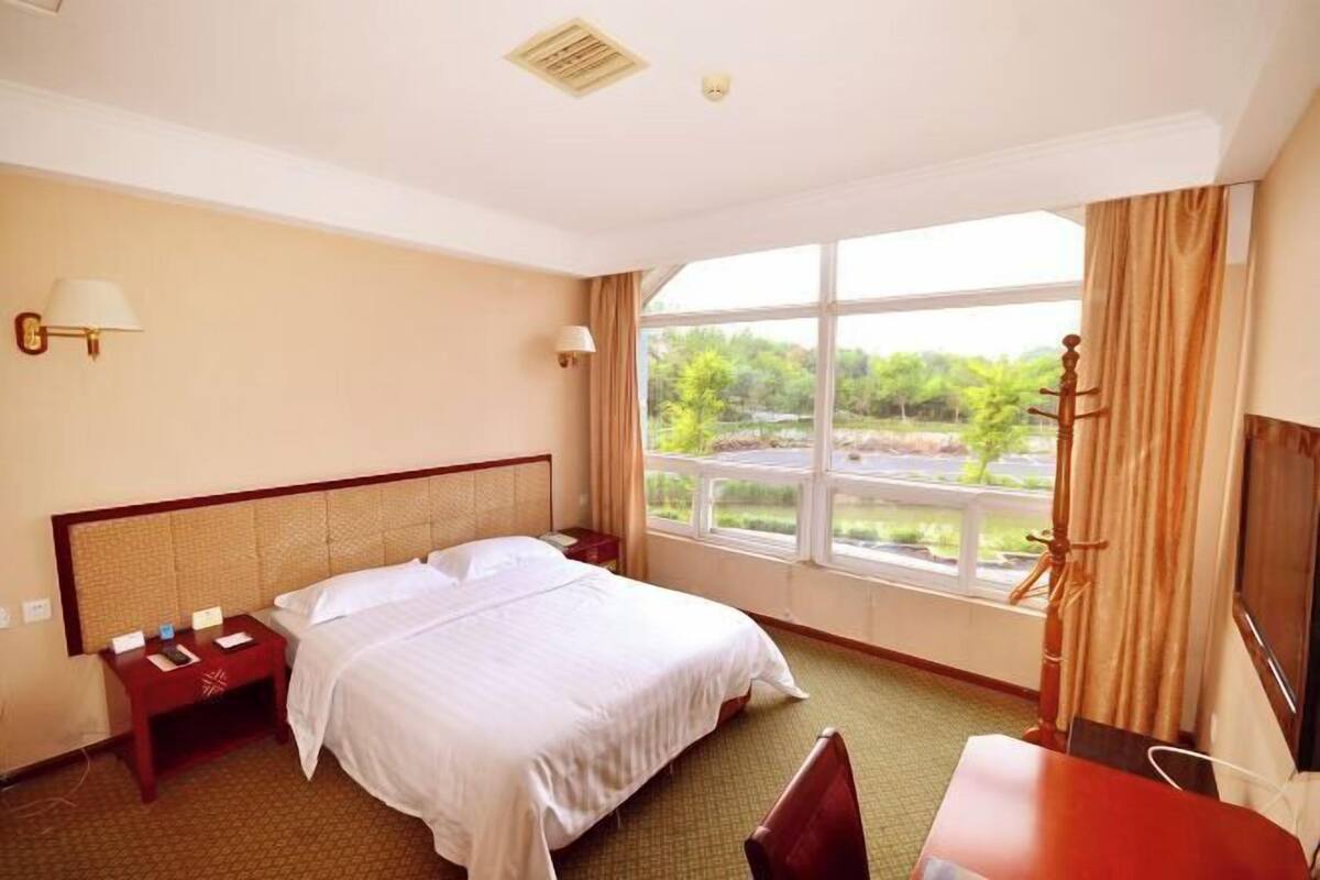 Hotelkamer met een bed, nachtkastjes, een bureau, een stoel, een televisie en een raam met uitzicht op groen.