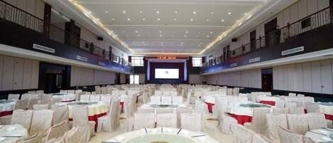 Un amplio salón de conferencias con mesas y sillas redondas, un balcón en un lateral y un escenario al frente.