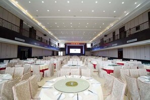 Een grote congreszaal met ronde tafels en stoelen, een balkon aan de zijkant en een podium aan de voorzijde.