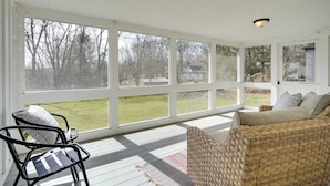 Eine überdachte Veranda mit einem Rattansofa, einem Metallstuhl und einem gemusterten Teppich.