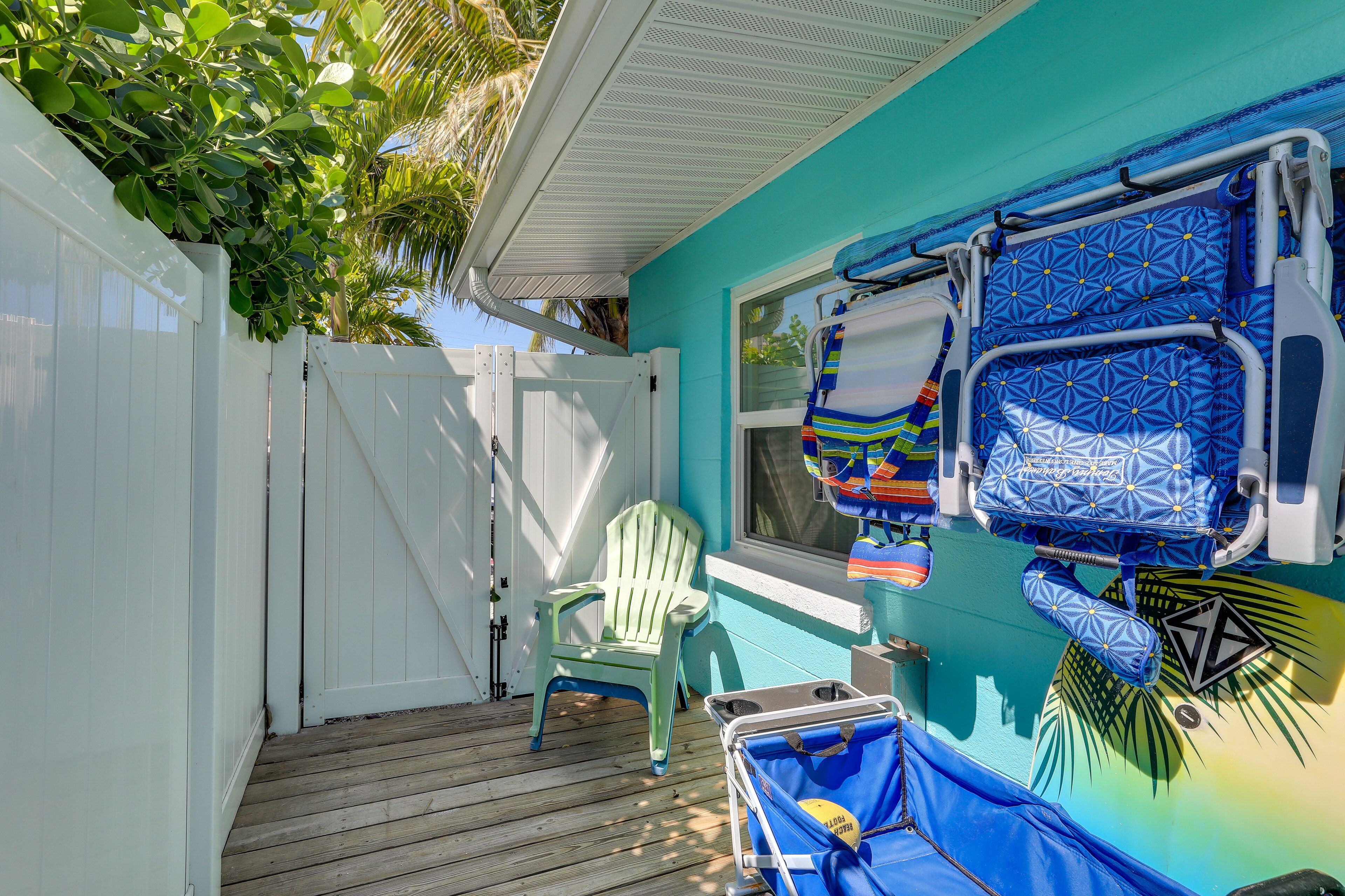 A room with a wooden deck, a green chair, a window with a view, and a blue wall with a hammock and a towel rack.