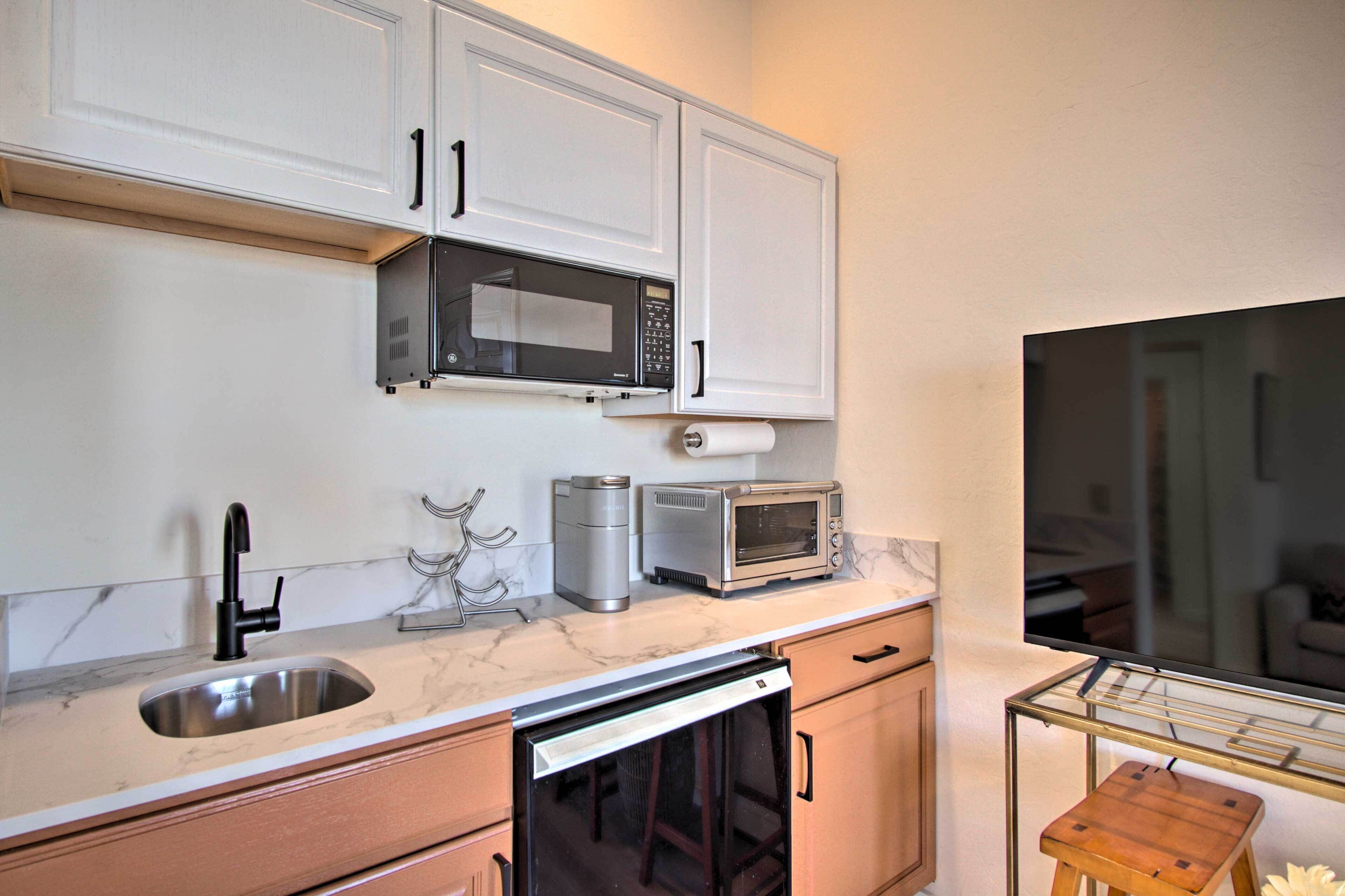 A compact kitchen with white cabinets, a stainless steel sink, a microwave, a toaster, and a dishwasher.