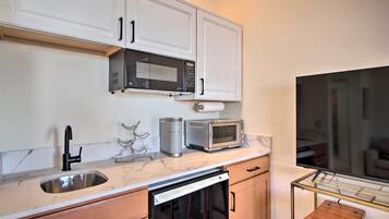 A compact kitchen with white cabinets, a stainless steel sink, a microwave, a toaster, and a dishwasher.