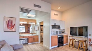 Una sala moderna con un sofá, una zona de comedor con televisor y una cocina con alacenas y microondas.