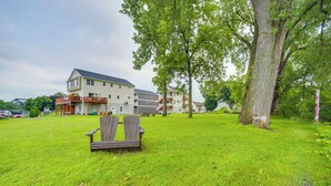 Un espace verdoyant avec un banc en bois, un grand arbre et, au fond, un immeuble à plusieurs étages doté de balcons.