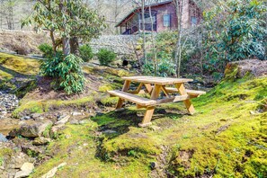 Ein rustikaler Holztisch für ein Picknick in einer natürlichen Umgebung, mit einem Steinhaus im Hintergrund.