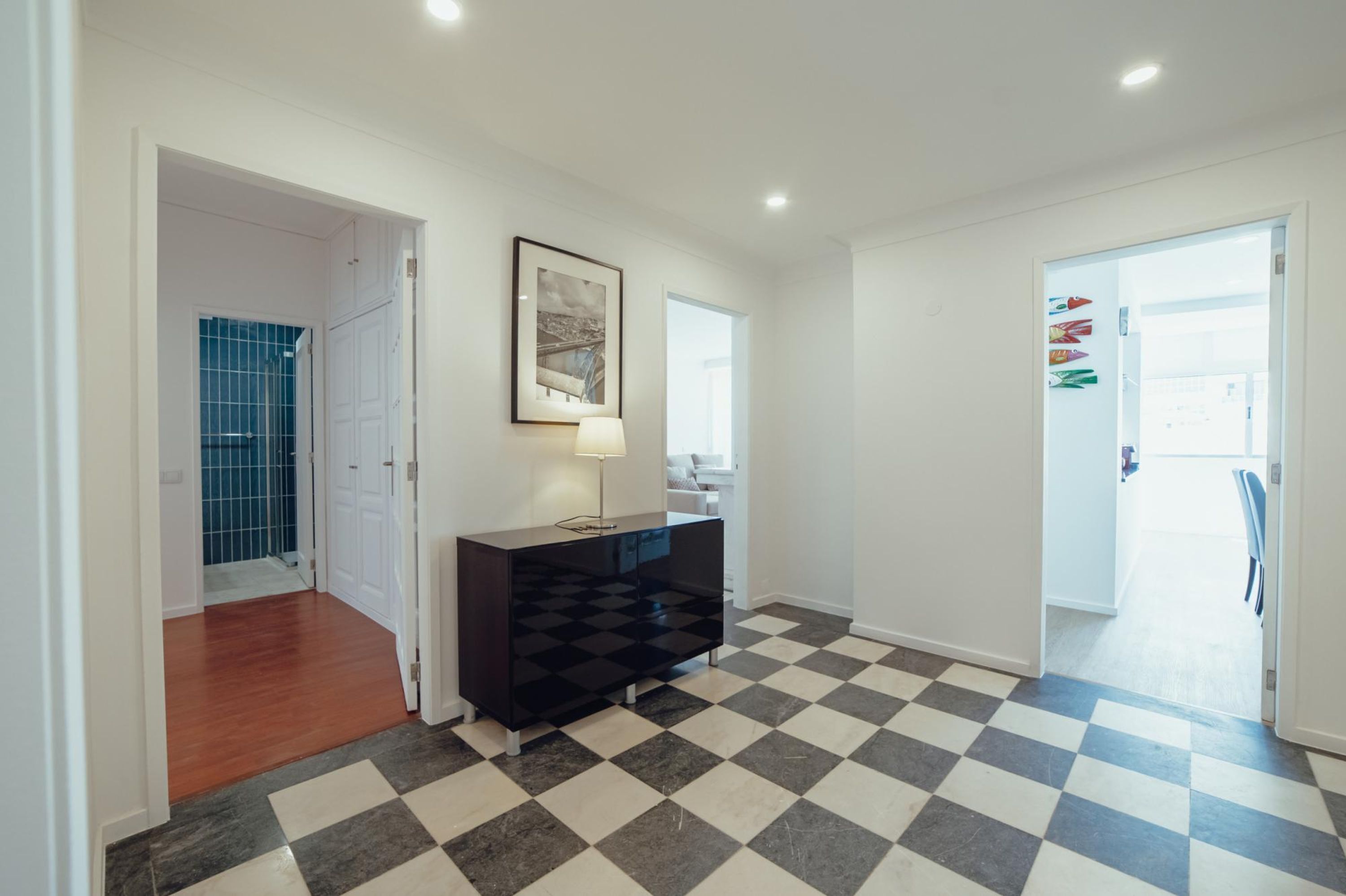 A hallway with a black and white checkered floor, a black console table with a lamp, and a framed picture on the wall.