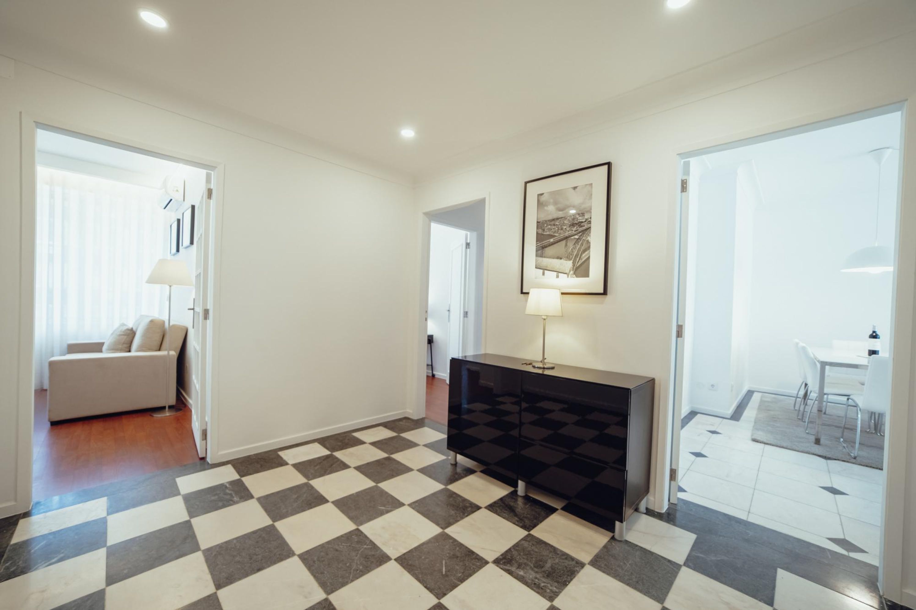 A modern interior with a checkered floor, a black console table, a framed picture, and a dining area with chairs and a table.